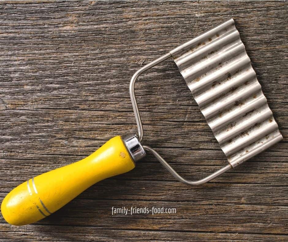 Crinkle cutter with yellow handle, on a wooden background.