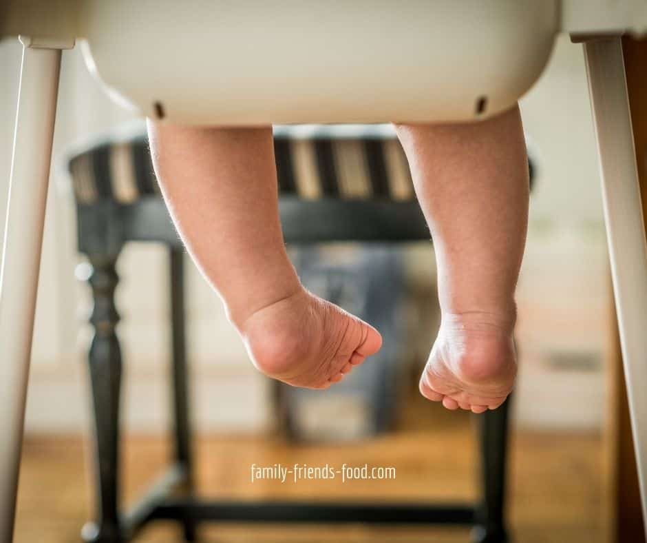 Rear view of lower half of a high chair, showing baby's legs.