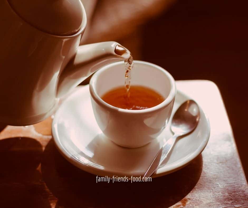 Tea pouring from a teapot into a cup on a saucer.