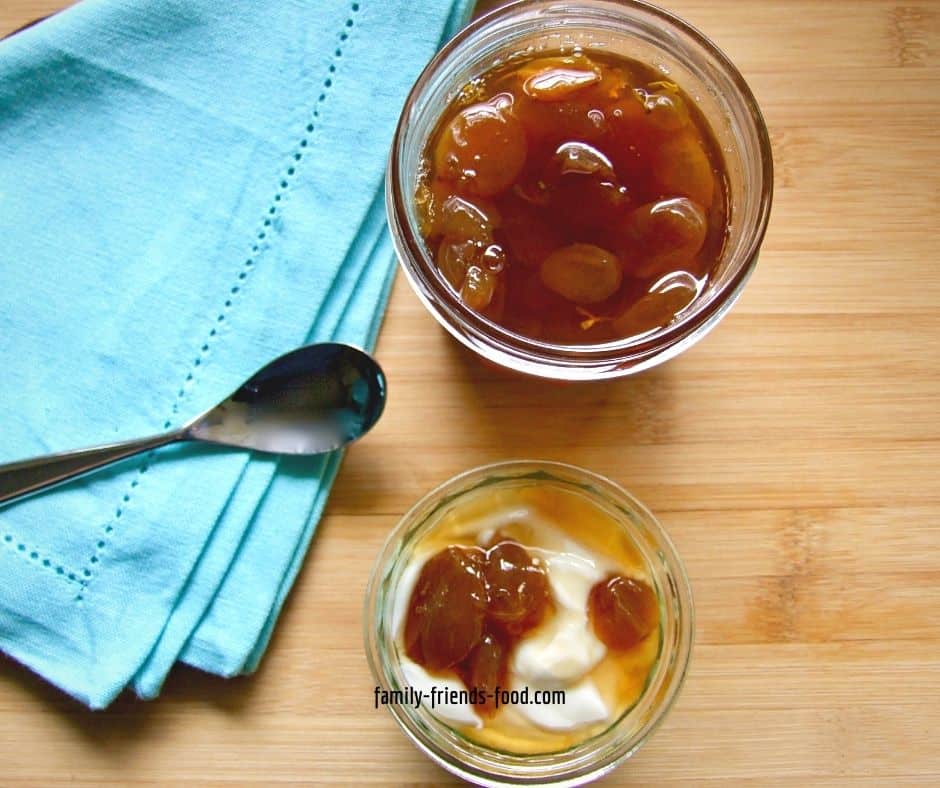 Overhead photo of an open jar of grape jam, and a bowl of yogurt with grape jam on top, + a napkin and spoon.