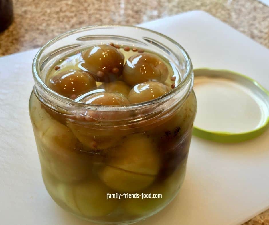 Open jar of pickled plums in brine.