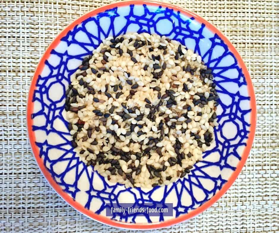 Black and white sesame seeds in a round blue and white dish, on a woven mat.