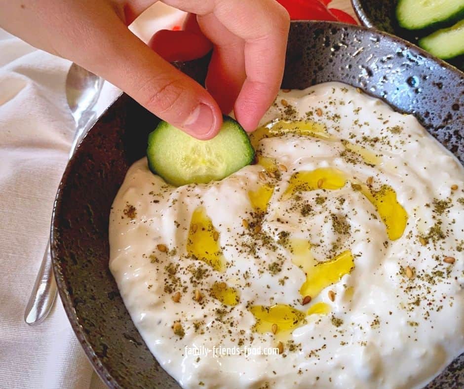 Hand dipping a slice of cucumber into a bowl of feta cheese dip.