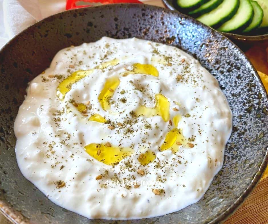 Close up of feta cheese dip with a drizzle of olive oil and a sprinkle of za'atar, in a black bowl.