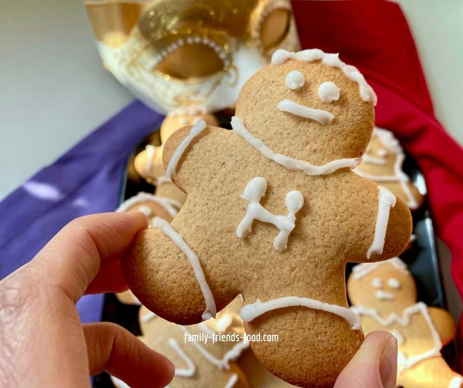 Fingers holding a gingerbread man iced with the letter 'H' for Haman.