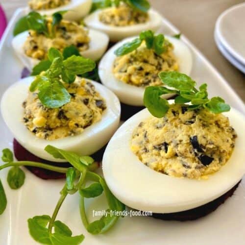 6 olive stuffed eggs on a white rectangular plate, garnished with watercress.