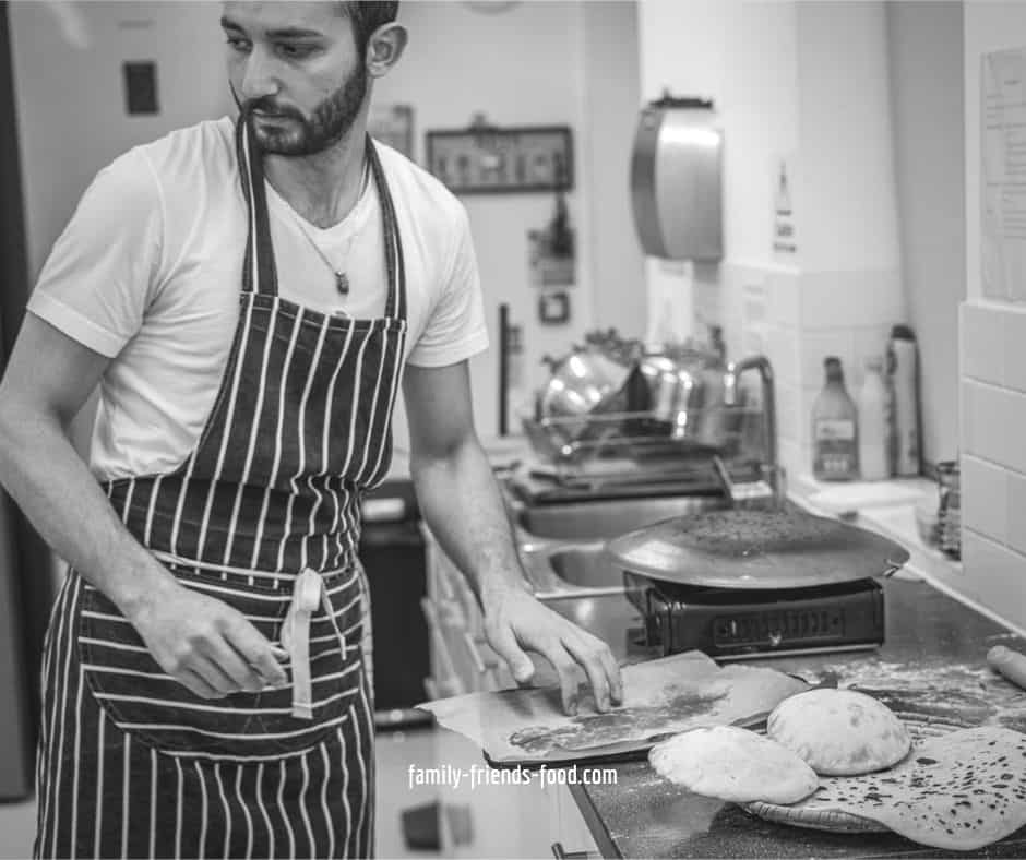 Black and white image of Faraj wearing a striped apron, in a kitchen.