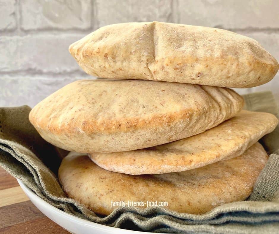 A stack of four wholewheat pita breads in a white bowl lined with a dark green cloth.