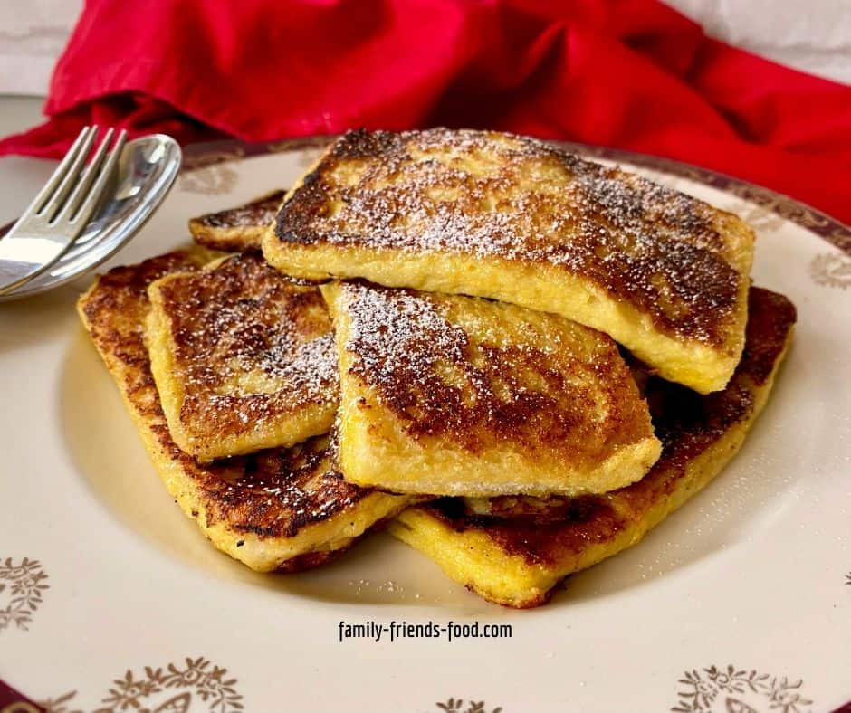 A stack of French toast slices on a fancy plate with spoon and fork, red napkin in background.