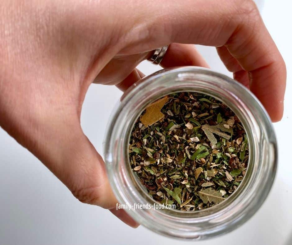 A hand holding an open jar of spice rack herb and spice blend for salmon, seen from above.