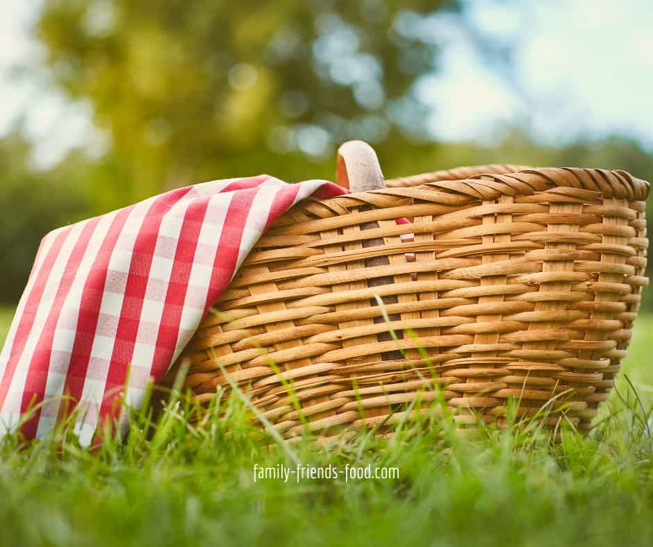 A picnic basket with a red and white checked cloth, sitting on the grass.