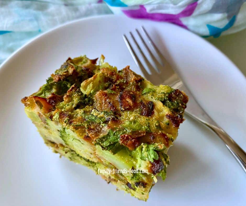 Close up image of a slice of broccoli kugel on a white plate with a fork.