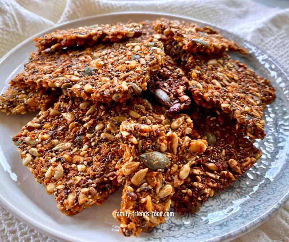 Pieces of seed and nut brittle on a grey and white plate. The plate rests on a textured white cloth.